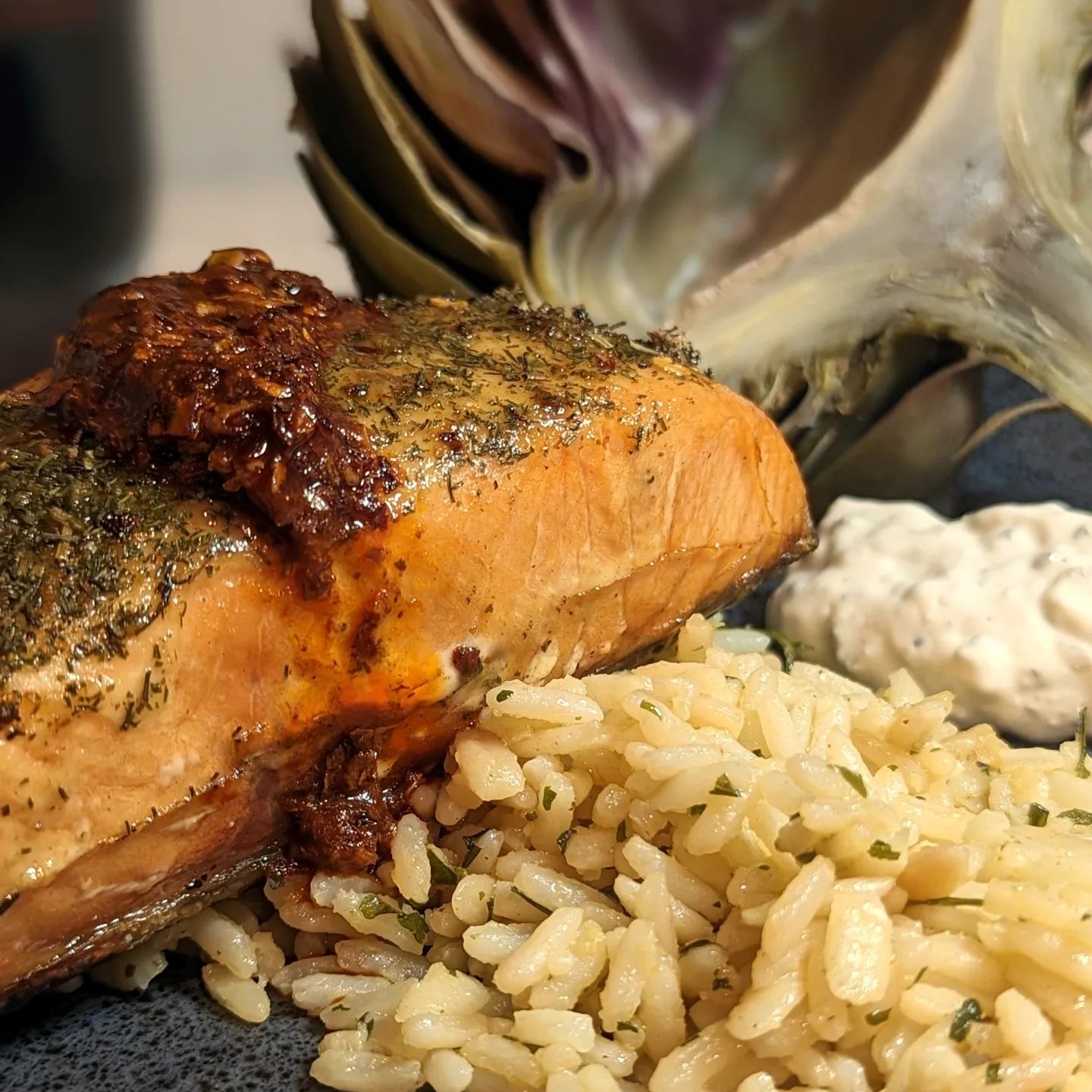 Grilled Salmon over garlic and herb rice with artichokeThis is not a keto dish, this was cooked for my wife, who does not eat keto. The salmon was brushed in a dill mustard and seasoned with @spiceology over easy. It was then grilled at 350 over the open flame of my Yoder Smoker using @bearmountainbbq cherry wood pellets. When the salmon was done it was topped with a touch of chili crisp for a bit of added texture and flavor, layering those flavors!The artichoke was steamed and seasoned with a no salt seasoning from Costco. Served with a side of @laterrafina tzatziki feta dip. The rice was leftover from a dinner she had made the night before and was simply warmed. This is my entry for #thequenion fish dish challenge! #salmon #fishdinner #seafood #gourmetfood #foodphotography #healthyrecipes #finedining #bearmountainbbq