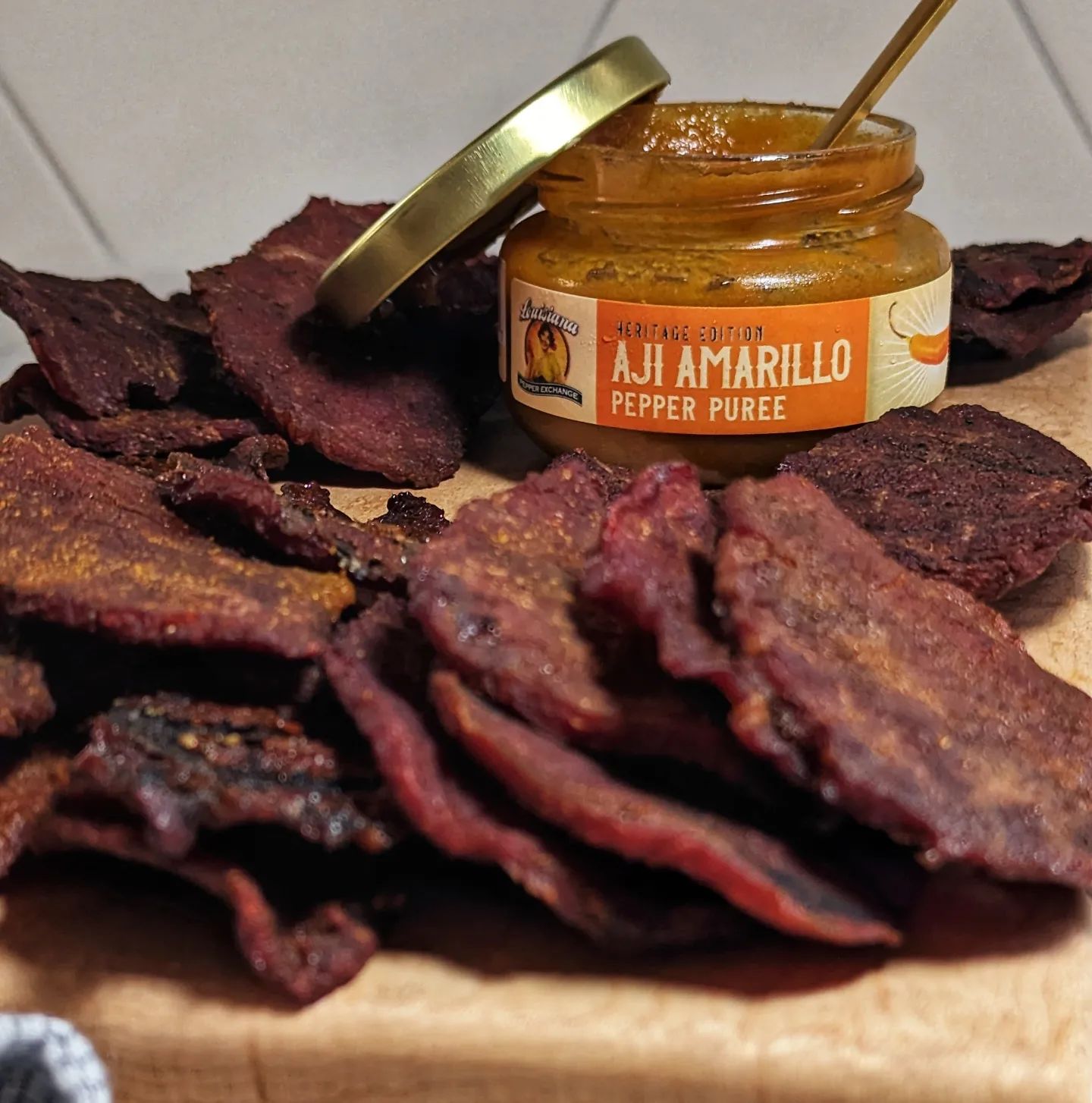 Aji Amarillo Beef JerkyThis spicy beef jerky will keep you coming back for more! @pepperexchange Aji Amarillo limited edition pepper puree is perfect for your next batch of beef jerky! Ingredients:2lb Eye of Round(1/4in slices)4oz Aji Amarillo2oz Soy Sauce2oz Worcestershire sauce8oz Bourbon Instructions: * Remove any exterior fat and slice the eye of round into thin slices, between 1/8 and 1/4 inch thick depending on your preference and place in a Ziploc bag. * Combine 2oz(half a jar) of Aji Amarillo, soy sauce, Worcestershire sauce, and bourbon. * Pour marinade into the bag and massage it into the sliced meat. * Let rest refrigerated overnight * Smoke on your smoker's lowest setting (usually about 2-3 hours) until you can bend the meat and it will show white cracks but not snap in half. Tip!! * For a bit of added heat, brush a thin layer of the Aji Amarillo onto each slice after placing it on the smoker (should use the remaining 2 oz)If any moisture remains on the surface when the jerky is done pat dry with a paper towel and store in a cool dry place for up to a week. Let's be honest though, it isn't likely going to be stored for a week, you'll be making a second batch by then! #pepperpartner #ajiamarillo #beefjerky #spicyfood #recipes #limitededition #snacktime #snackideas